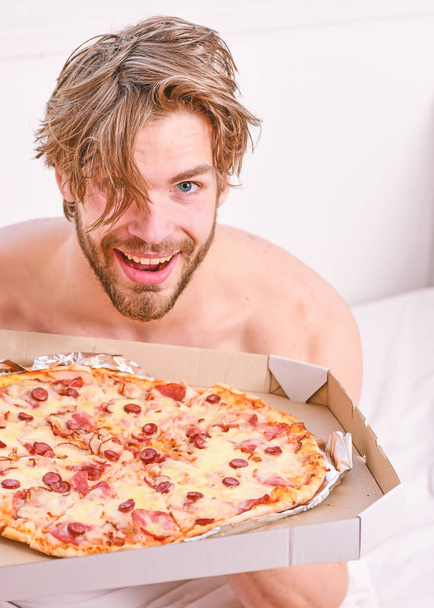 Man likes pizza for breakfast. Sexy man eat pizza lying on bed. Portrait of lazy muscular man eating pizza while laying on a bed at home. Home pizza. - Foto, Imagem
