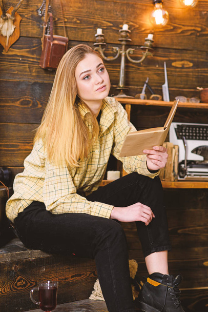 Girl student study with book in house of gamekeeper. Study concept. Lady on calm face in plaid clothes looks cute and casual. Girl in casual outfit sits with book in wooden vintage interior - Foto, afbeelding