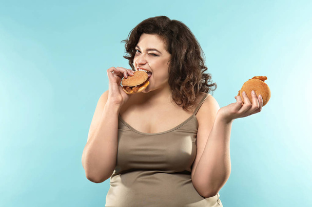 Надмірна вага жінки з гамбургерами на кольоровому фоні
 - Фото, зображення