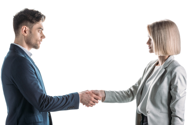 pretty businesswoman and handsome businessman shaking hands and looking at each other isolated on white - 写真・画像