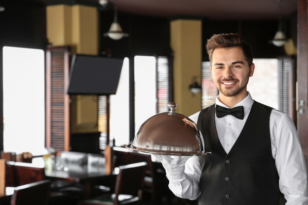 Camarero joven con bandeja y cloche en restaurante
 - Foto, imagen