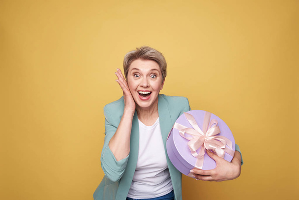 Half length of surprised mother holding presents on yellow background - Fotoğraf, Görsel