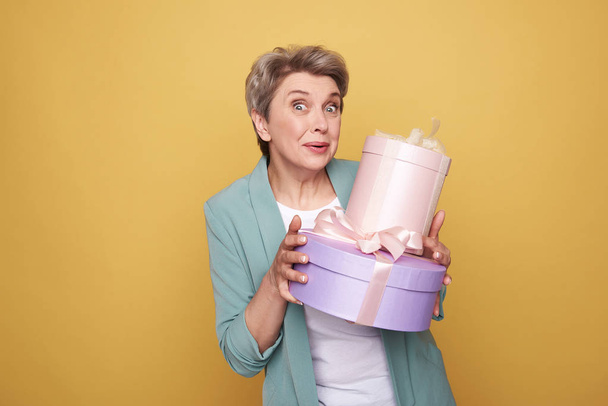 Half length of surprised mother holding presents on yellow background - Fotoğraf, Görsel