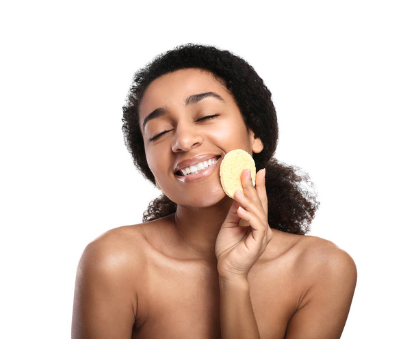 Joven mujer afroamericana con maquillaje quitando esponja sobre fondo blanco
 - Foto, imagen