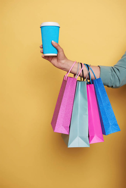 Cropped photo of female hand holding colorful shopping bags and a cupholder - Foto, afbeelding