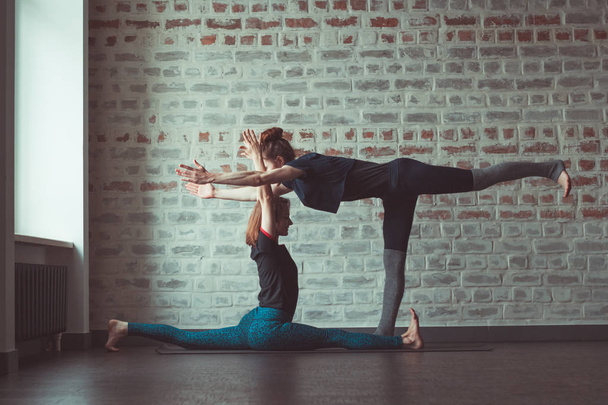 two beautiful caucasian women doing partner yoga in yoga studio opposite brick wall - Fotó, kép
