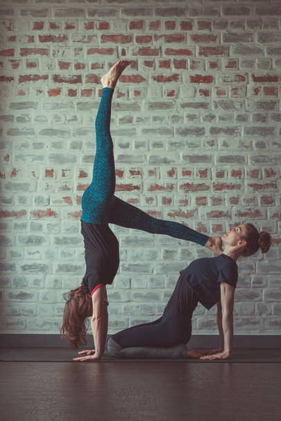 two beautiful caucasian women doing partner yoga in yoga studio opposite brick wall - Foto, afbeelding
