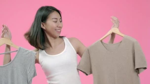 Młoda piękna modna Azjatycka kobieta wybiera ubrania w nieformalnej odzieży na różowym tle strzał studio. Szczęśliwy uśmiechnięty godny podziwu kobieta cieszy się sukcesem. - Materiał filmowy, wideo