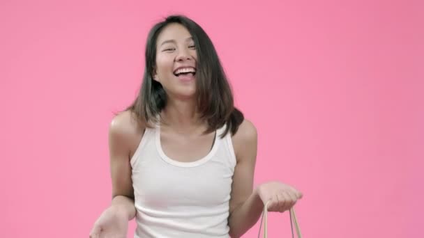Młoda piękna modne Asian kobieta trzyma torby na zakupy uczucie szczęśliwy uśmiechając się w casual Odzież nad różowe tło strzał studio. Szczęśliwy uśmiechnięty godny podziwu kobieta cieszy się sukcesem. - Materiał filmowy, wideo