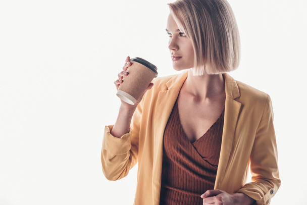 beautiful blonde woman holding disposable cup and looking away on grey - Valokuva, kuva