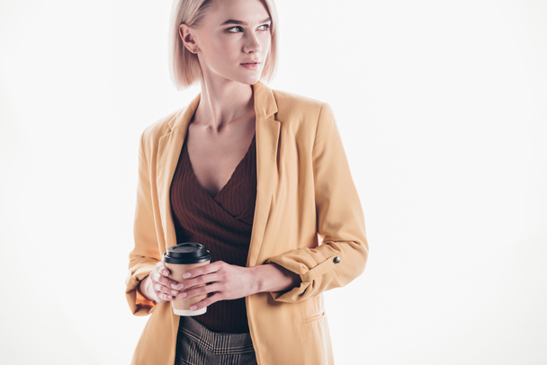 attractive, trendy woman with blonde hair holding coffee to go and looking away on grey - Fotografie, Obrázek