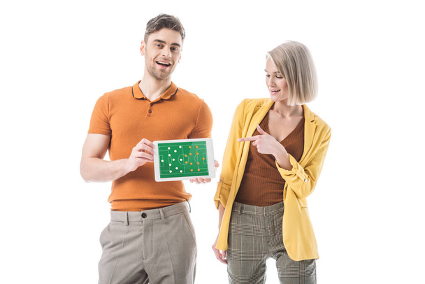 hymyilevä mies tilalla digitaalinen tabletti jalkapallo peli sovellus ruudulla, kun seisoo lähellä nainen osoittaa sormella eristetty valkoinen
 - Valokuva, kuva