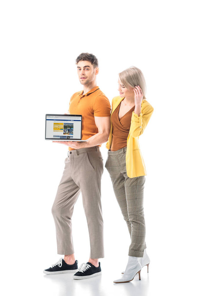 handsome man holding laptop with booking website on screen while standing near pretty woman isolated on white - Zdjęcie, obraz