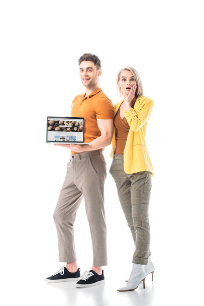 cheerful man holding laptop with depositphotos website on screen while standing near surprised woman isolated on white - Φωτογραφία, εικόνα