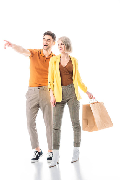 handsome man pointing with finger while standing near pretty woman with paper bags isolated on white - Foto, immagini