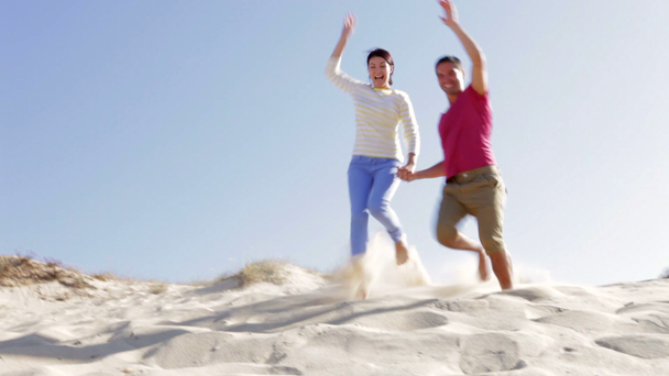 Couple in casual clothing running down sand dune - Filmati, video