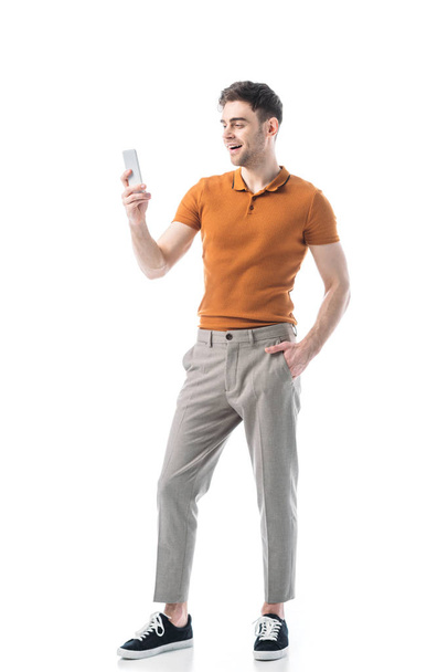 good-looking cheerful man with hand in pocket using smartphone isolated on white - Фото, зображення