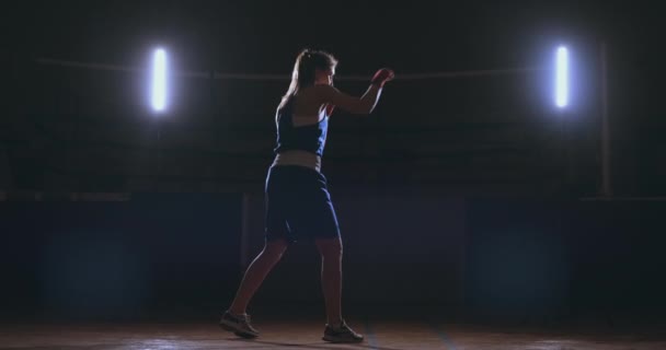 Kaunis nainen nyrkkeilijä harjoittelee pimeällä kuntosalilla ja treenaa lyöntejä hidastettuna. sivukuva. Steadicam laukaus
 - Materiaali, video