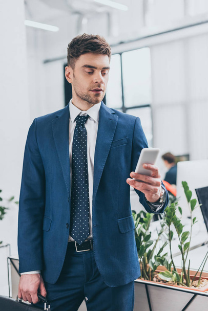 handsome, serious businessman using smartphone in office - Photo, image
