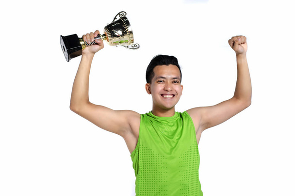 Boldog kifejezés fiatal ember beleférjen sportruházat, gazdaság arany trófeát, mint fehér háttér - Fotó, kép
