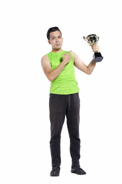 Full body length portrait of young fit man in sportswear , standing and holding gold trophy over white background - Photo, Image