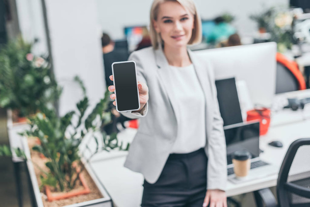 selective focus of pretty blonde businesswoman holding smartphone with blank screen - Fotó, kép