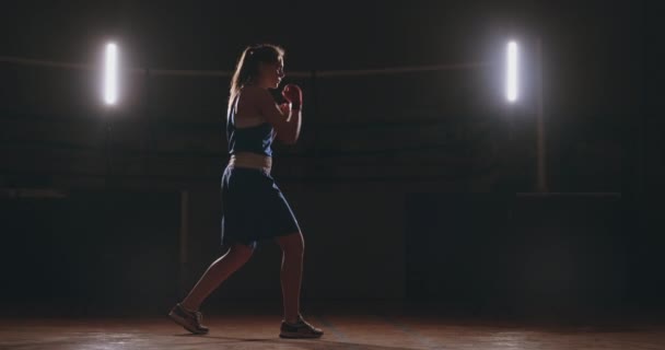 Kaunis nainen nyrkkeilijä harjoittelee pimeällä kuntosalilla ja treenaa lyöntejä hidastettuna. Kamera liikkeen puolella View. Steadicam laukaus
 - Materiaali, video
