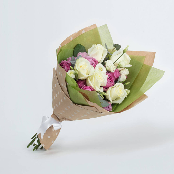 Um buquê de belas rosas brancas e flores rosa em um pacote artesanal em um fundo cinza
 - Foto, Imagem