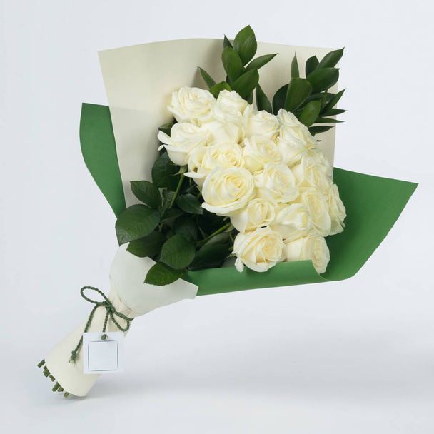 Boeket van mooie bloemen van witte rozen in kleurrijke groene verpakking op een grijze achtergrond - Foto, afbeelding