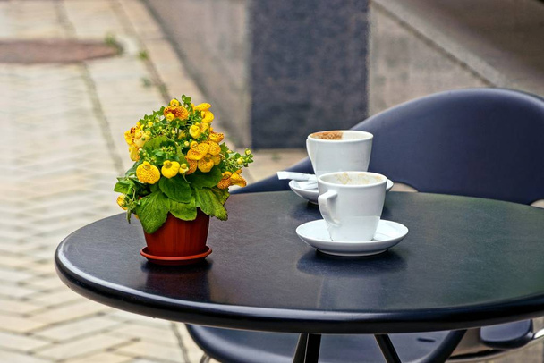 Pyöreä muovipöytä kadulla kahvilassa tyhjiä kuppeja ja kukkaruukku
 - Valokuva, kuva
