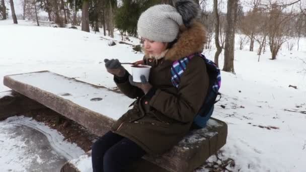 Mała dziewczynka siedzi na ławce w parku i jedzenie pudding czekoladowy - Materiał filmowy, wideo