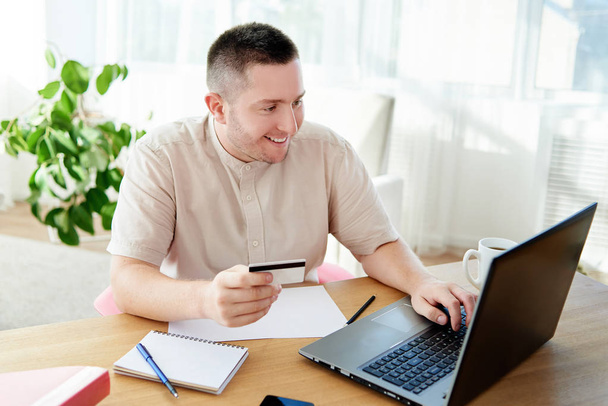 Happy smiling man booking hotel on laptop with credit card at home office, copy space. Technology, banking, paying, online shopping concept - 写真・画像