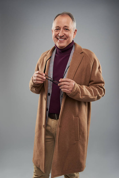 Cheerful man in long coat standing alone and holding glasses - Foto, Imagen