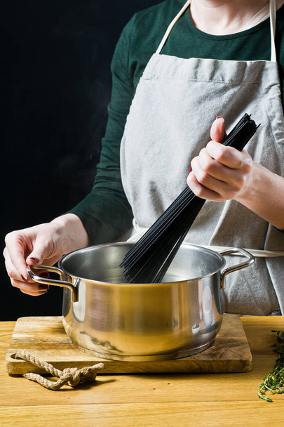 Шеф-повар кладет черные спагетти в кипящую воду. Чёрный фон
 - Фото, изображение