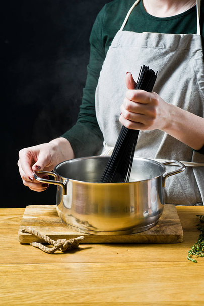 Шеф-повар кладет черные спагетти в кипящую воду. Чёрный фон
 - Фото, изображение