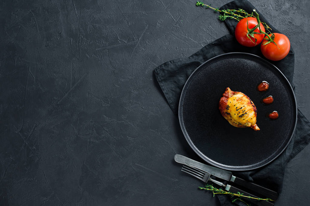 Calamar al horno en salsa de tomate en un plato negro. Fondo negro
,  - Foto, imagen