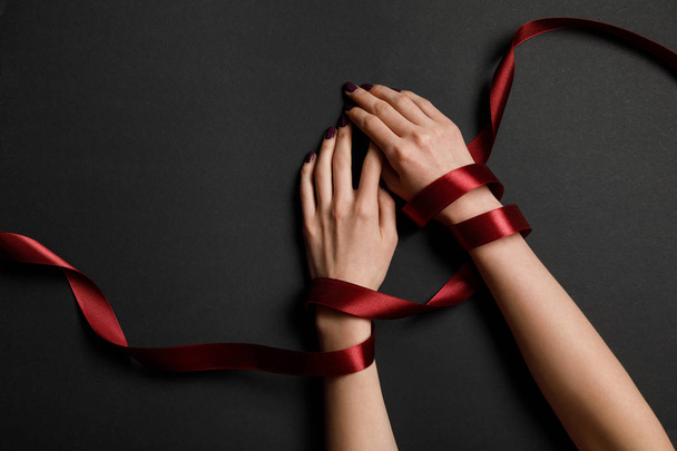 partial view of female hands in satin red ribbon on black background - Zdjęcie, obraz