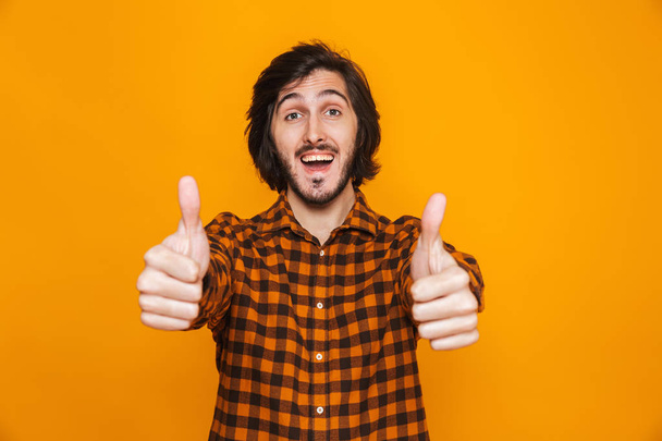 Handsome young happy man isolated over yellow wall background showing thumbs up. - Foto, Imagen