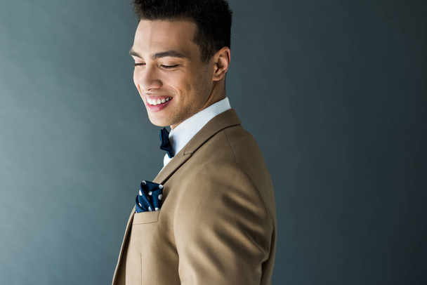 stylish mixed race man in suit and bow tie smiling isolated on grey with copy space - Fotografie, Obrázek