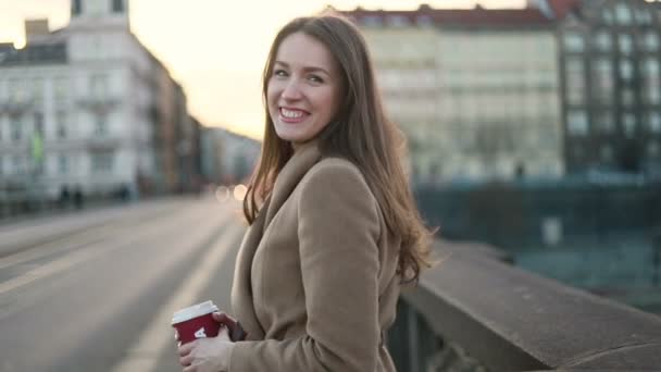 drinks and people concept - happy young woman or teenage girl drinking coffee from paper cup sitting on on city street bench - Materiał filmowy, wideo