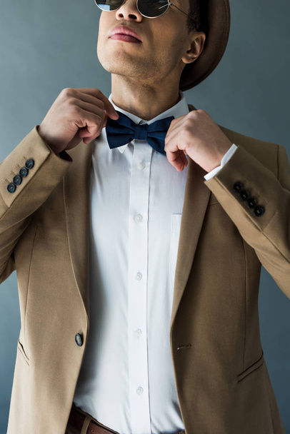 partial view of stylish mixed race man in suit adjusting bow tie isolated on grey - Fotografie, Obrázek