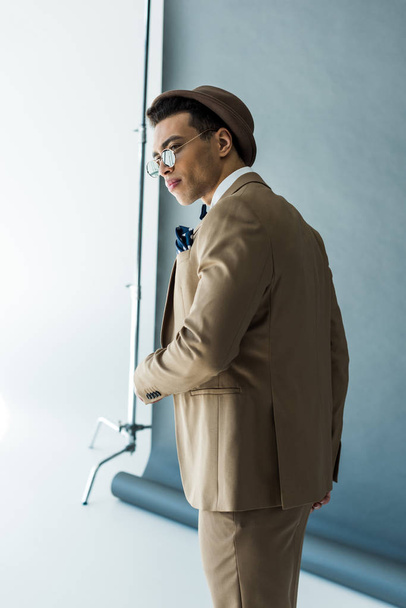 fashionable mixed race man in suit and hat posing on grey - Foto, afbeelding