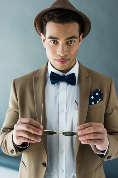 stylish mixed race man in suit and bow tie looking at camera on grey - Fotó, kép