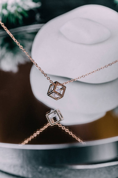 A close-up of a gold chain with a pendant in the shape of a diamond, a pebble inside the pendant, hangs over the glass surface. The concept of jewels. - Photo, Image