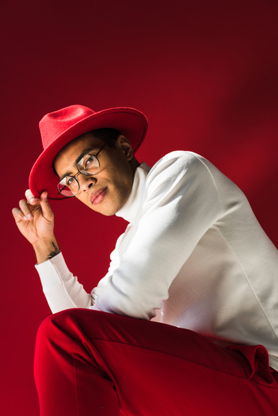 matala kulma näkymä tyylikäs sekoitettu rodun mies hattu ja lasit istuu ja poseeraa punainen
 - Valokuva, kuva
