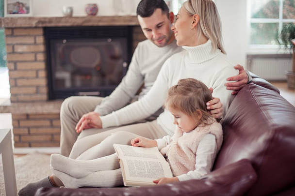 Belle jeune famille lit un livre près de la cheminée. Confortable
. - Photo, image