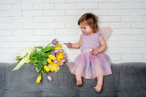 Pikkutyttö, jolla on tulppaanit keijujen vaatteissa, istuu sängyllä. Kevät mieliala
 - Valokuva, kuva