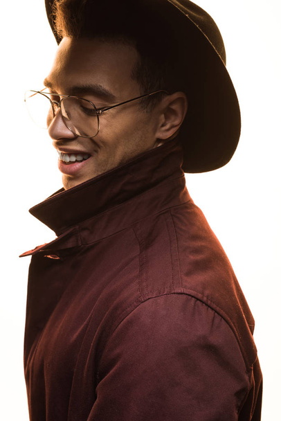 stylish mixed race man in glasses and hat smiling and posing isolated on white - Foto, afbeelding