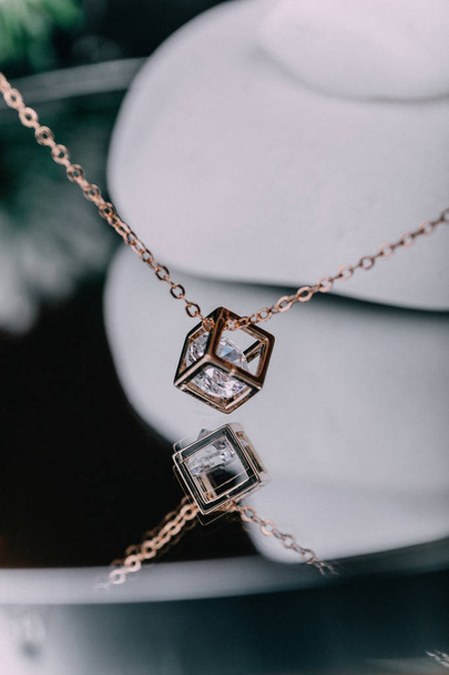 A close-up of a gold chain with a pendant in the shape of a diamond, a pebble inside the pendant, hangs over the glass surface. The concept of jewels. - Фото, зображення