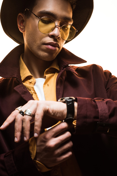 stylish mixed race man in hat and sunglasses putting on watch isolated on white - Photo, Image